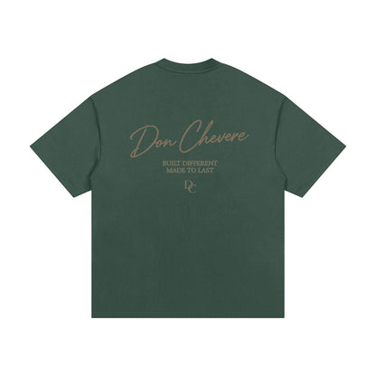 Don Chevere Essential Oversized Heavy Tee in dark green, 100% cotton with a round neck and short sleeves. Features a graphic print on the back.